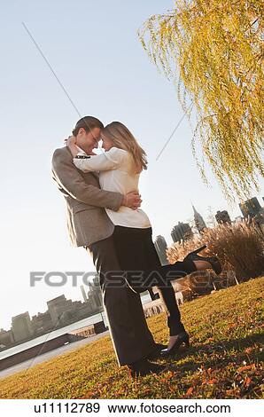 Stock Photo - USA, New York, Long Island City, Young couple embracing in park. Fotosearch