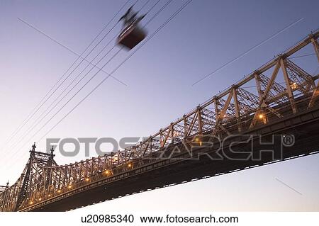 Stock Image - USA, New York, New York City, Manhattan, Queensboro Bridge, Overhead cable car at dusk. Fotosearch