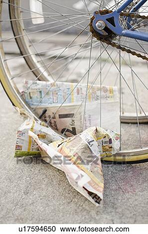 Stock Image - USA, New York State, New York City, Crumpled newspaper under bicycle wheel. Fotosearch