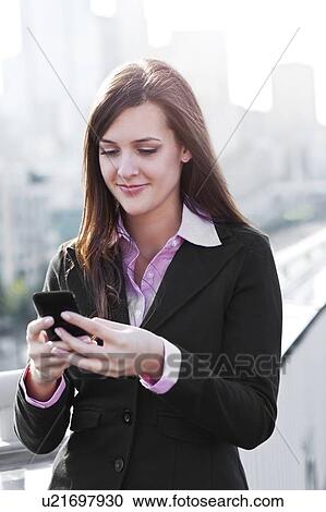 Stock Image - USA, Seattle, Smiling young businesswoman sending text message. Fotosearch