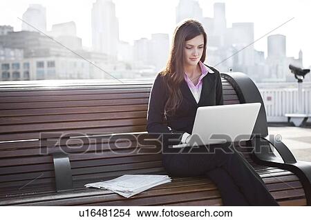 Picture - USA, Seattle, Young businesswoman working on laptop on bench. Fotosearch