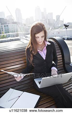 Stock Photo - USA, Seattle, Young businesswoman sitting on bench and working. Fotosearch