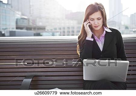 Stock Photo - USA, Seattle, Young businesswoman sitting on bench and working. Fotosearch