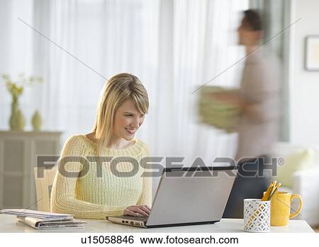 Woman working on laptop at home, man in background View Large Photo Image Stock Photograph - Woman working on laptop at home, man in background. Fotosearch