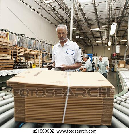 Stock Image - Worker inspecting bundle on conveyor belt. Fotosearch