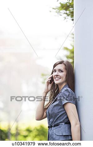 Stock Photo - Young elegant woman standing and talking via phone. Fotosearch