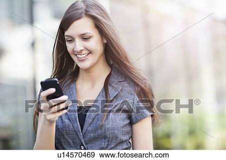 Stock Photo - Young elegant woman standing and using mobile phone. Fotosearch