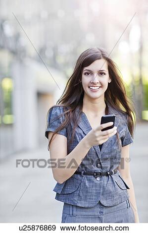Young elegant woman standing and using mobile phone View Large Photo Image Stock Photo - Young elegant woman standing and using mobile phone. Fotosearch