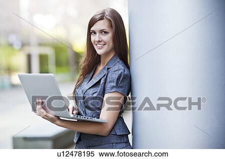Young elegant woman standing and using laptop View Large Photo Image Stock Photography - Young elegant woman standing and using laptop. Fotosearch