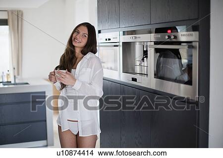 Picture - Young woman enjoying coffee in domestic kitchen. Fotosearch