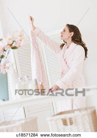 Picture - Young woman holding dress in bedroom. Fotosearch