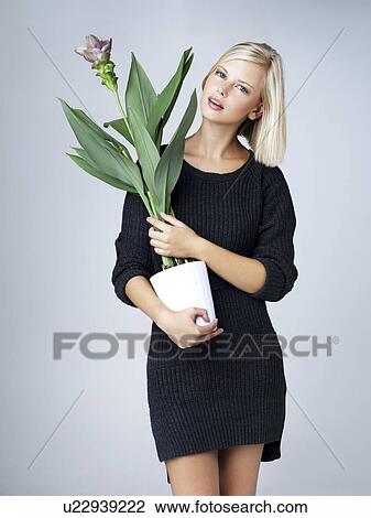 Stock Image - Young woman holding flowering plant, studio shot. Fotosearch