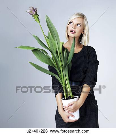 Young woman holding flowering plant, studio shot View Large Photo Image Stock Image - Young woman holding flowering plant, studio shot. Fotosearch