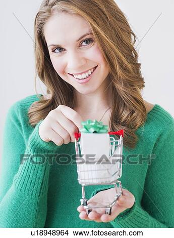 Picture - Young woman holding miniature shopping cart with gift box. Fotosearch