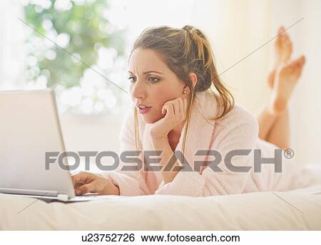 Young woman lying on bed in bathrobe with laptop View Large Photo Image Stock Photograph - Young woman lying on bed in bathrobe with laptop. Fotosearch