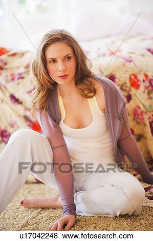 Stock Photo - Young woman sitting on floor in bedroom. Fotosearch