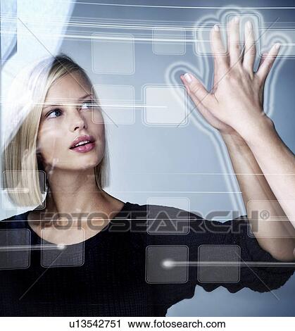 Stock Image - Young woman using futuristic touchscreen, studio shot. Fotosearch