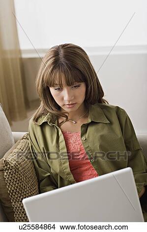 Picture - Young woman using laptop at home. Fotosearch