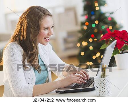Young woman working on laptop with Christmas tree on background View Large Photo Image Stock Image - Young woman working on laptop with Christmas tree on background. Fotosearch