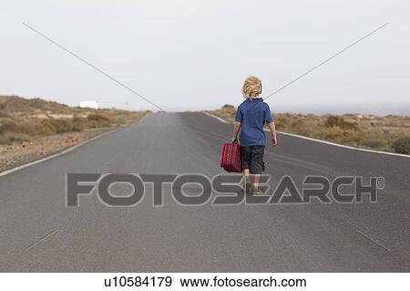 Stock Photo - Boy carrying suitcase on rural road. Fotosearch