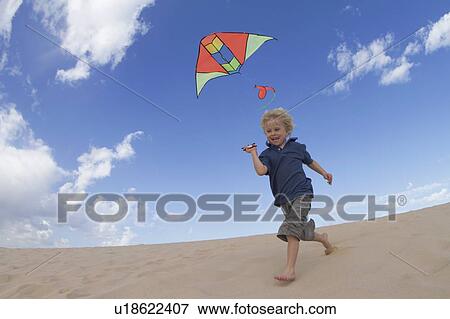 Stock Photo - Boy flying kite on sand dune. Fotosearch