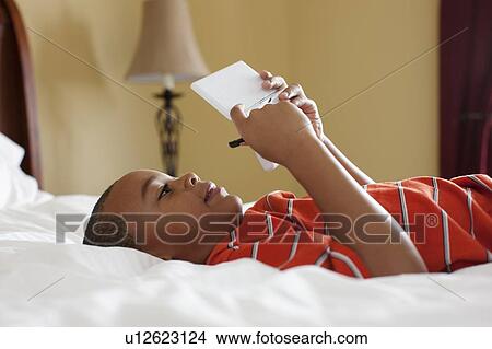 Boy playing handheld video game on bed View Large Photo Image Picture - Boy playing handheld video game on bed. Fotosearch