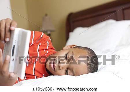 Boy playing handheld video game on bed View Large Photo Image Stock Photo - Boy playing handheld video game on bed. Fotosearch