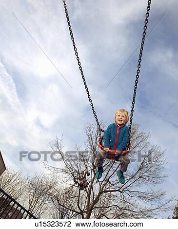 Stock Image - Boy playing in swing at park. Fotosearch