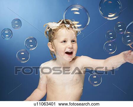 Stock Image - Boy popping bubbles in bath. Fotosearch