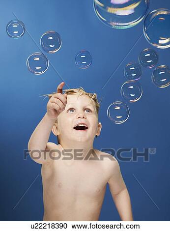 Stock Image - Boy popping bubbles in bath. Fotosearch