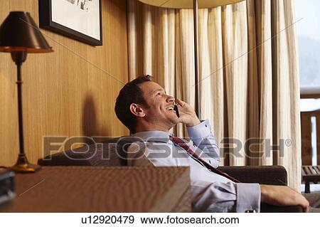 Stock Photo - Businessman on cell phone in hotel room. Fotosearch