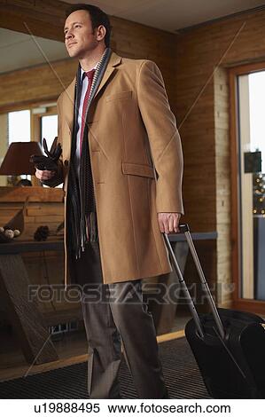 Stock Photography - Businessman rolling luggage in lobby. Fotosearch
