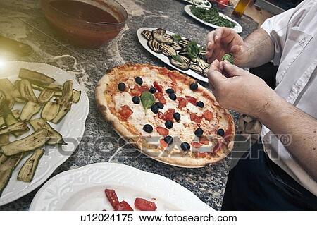 Stock Photography - Chef garnishing pizza in kitchen. Fotosearch