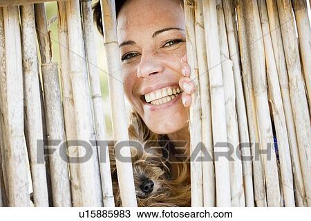 Stock Image - Close up of woman and dog behind fence. Fotosearch