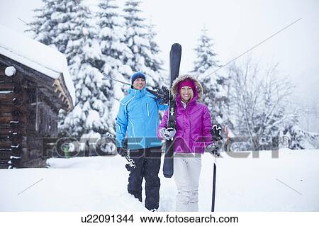 Picture - Couple carrying skis and poles in snow. Fotosearch