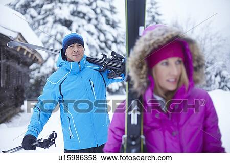 Stock Photo - Couple carrying skis and poles in snow. Fotosearch