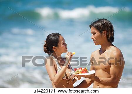 Stock Image - Couple eating together on beach. Fotosearch