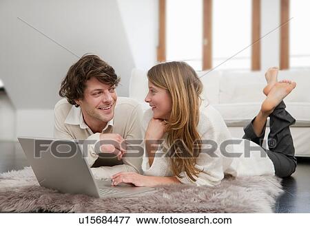 Stock Photo - Couple using laptop together on rug. Fotosearch