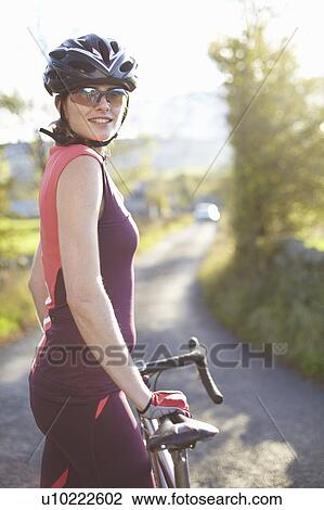 Stock Image - Cyclist standing on rural road. Fotosearch