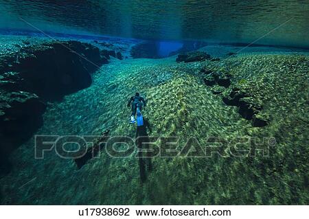Stock Image - Diver swimming by rock formations. Fotosearch