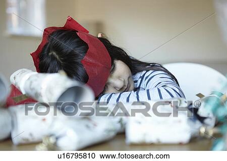 Stock Image - Girl in paper crown sleeping at desk. Fotosearch