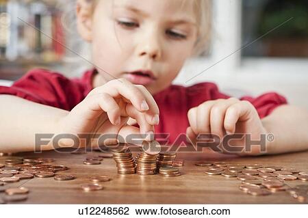 Stock Image - Girl playing with pennies at table. Fotosearch