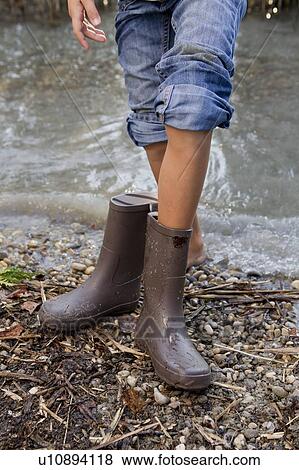 Stock Photo - Girl taking off rain boots by pond. Fotosearch