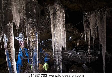 Stock Image - Hiker with icicles in glacial cave. Fotosearch