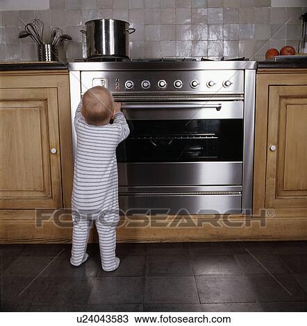 Stock Image - Infant standing by oven in kitchen. Fotosearch