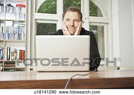 Stock Image - Man at computer with chin in hands. Fotosearch