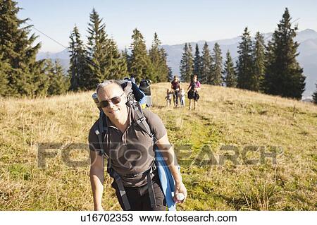 Stock Image - Man hiking with pack on grassy hillside. Fotosearch