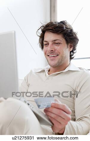 Stock Image - Man shopping online in living room. Fotosearch