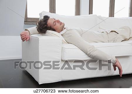 Stock Image - Man sleeping on sofa in living room. Fotosearch
