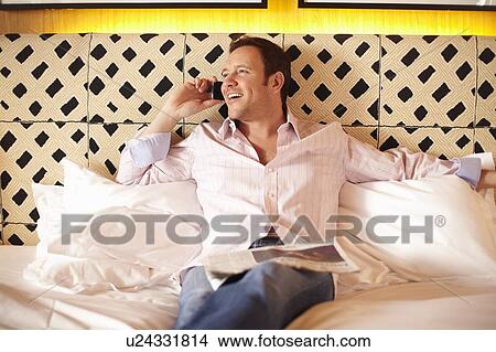 Picture - Man talking on cell phone on bed. Fotosearch